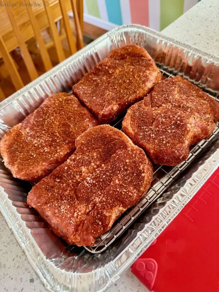 Four seasoned pork collars, setting on a cookie cooling sheet in a disposable aluminum pan