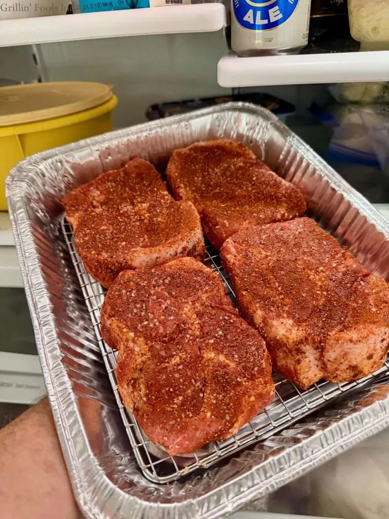 Four seasoned pork collars in an aluminum pan heading into the fridge to dry brine for a couple hours.