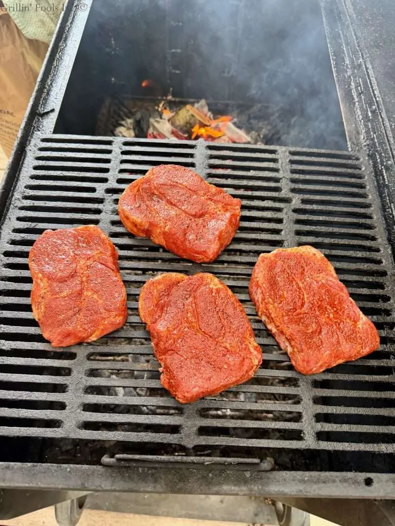 Four seasoned pork collars on the cool, near side of the grill while coals burn on the far side of the grill