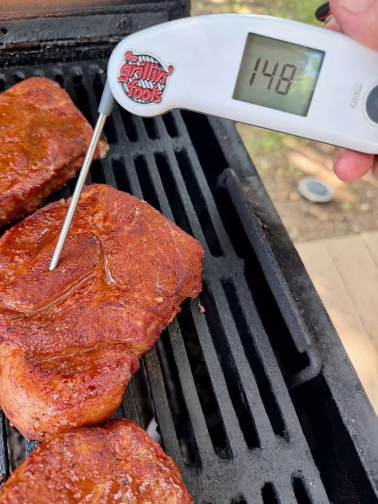 A probe thermometer reading 148F on a charcoal grill