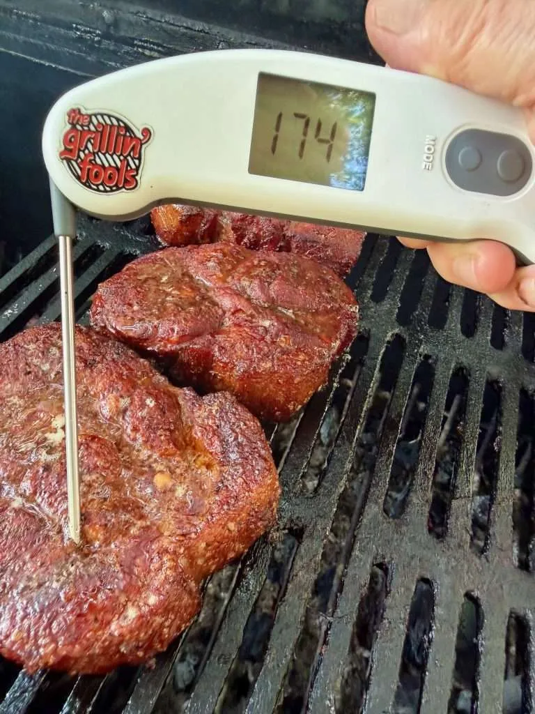 A probe thermometer reading 174F on a charcoal grill