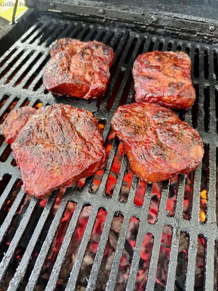 Four pork collars over a bed of hot coals on a charcoal grill