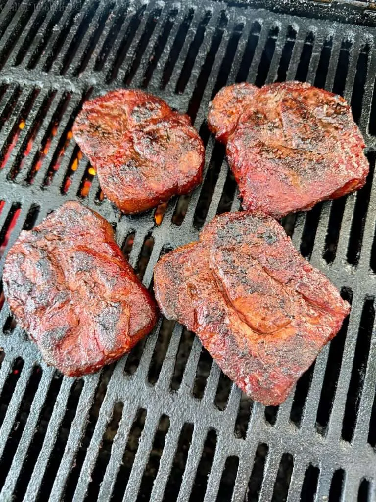 Four pork collars off to the side of the grill with no heat after getting charred a bit over the hot coals