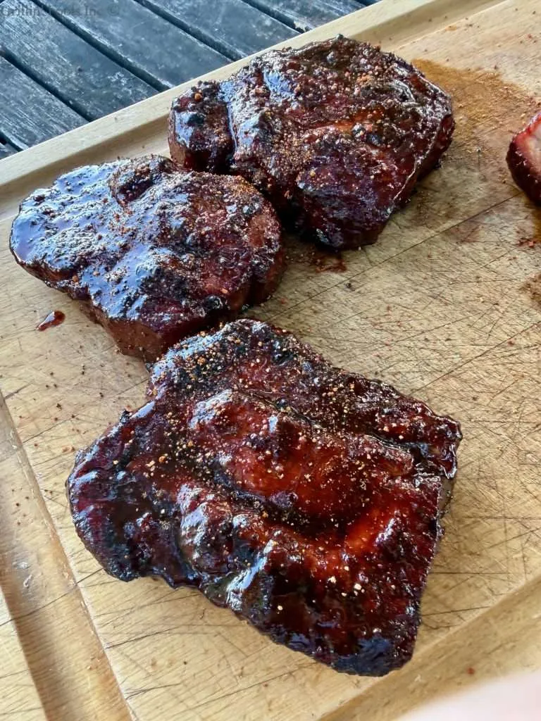 Saucy pork collar, dusted with BBQ rub on a wooden cutting board.