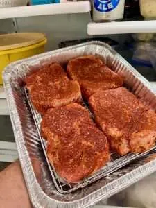 Four seasoned pork collars in an aluminum pan heading into the fridge to dry brine for a couple hours.