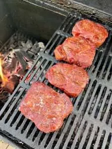 A line of four pork collars just off the edge of the hot coals in a charcoal grill