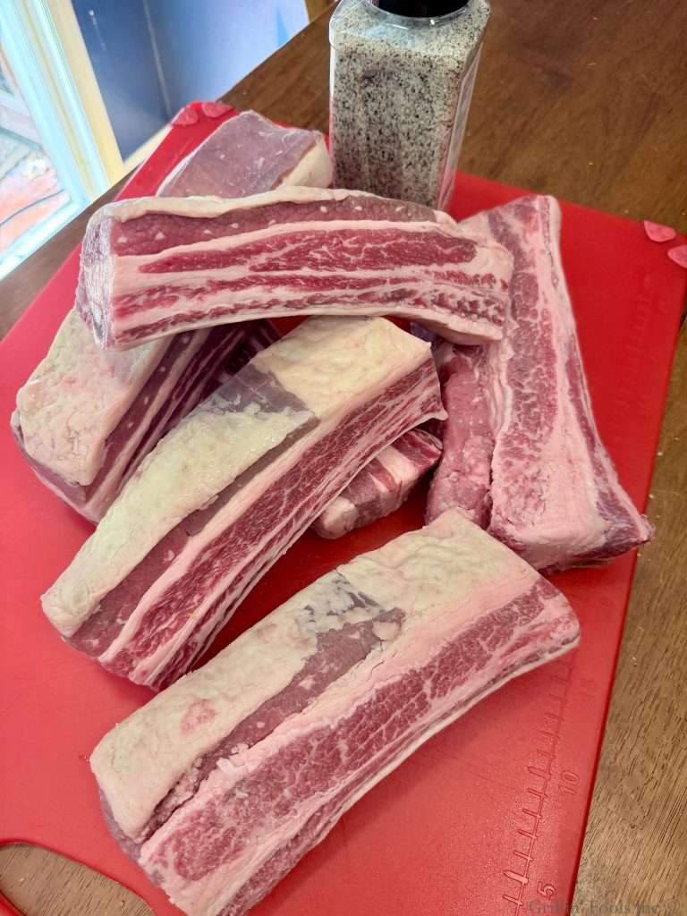 A pile of six raw, English cut beef ribs on a red cutting board