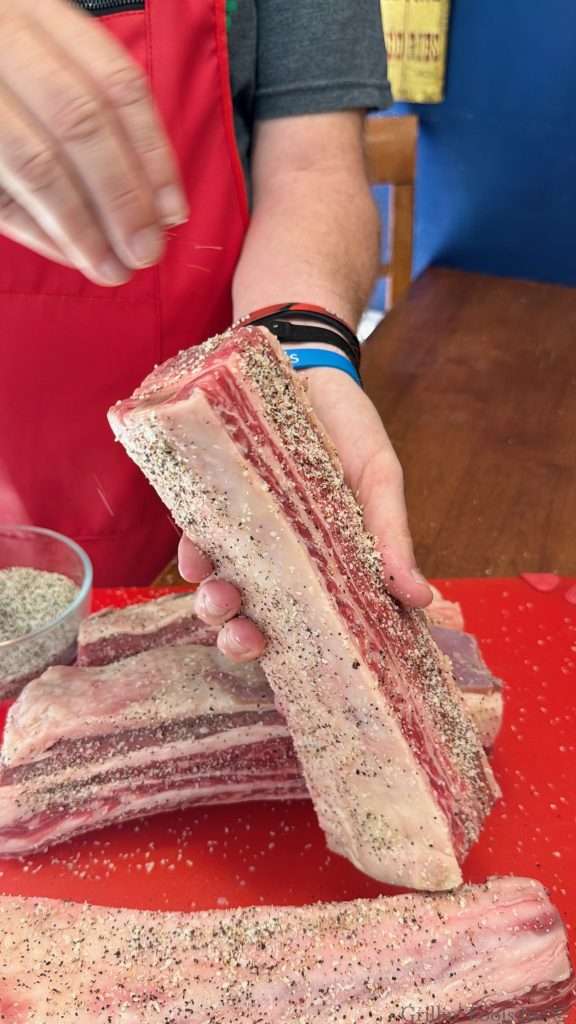 A man seasons the ends of an English cut beef rib