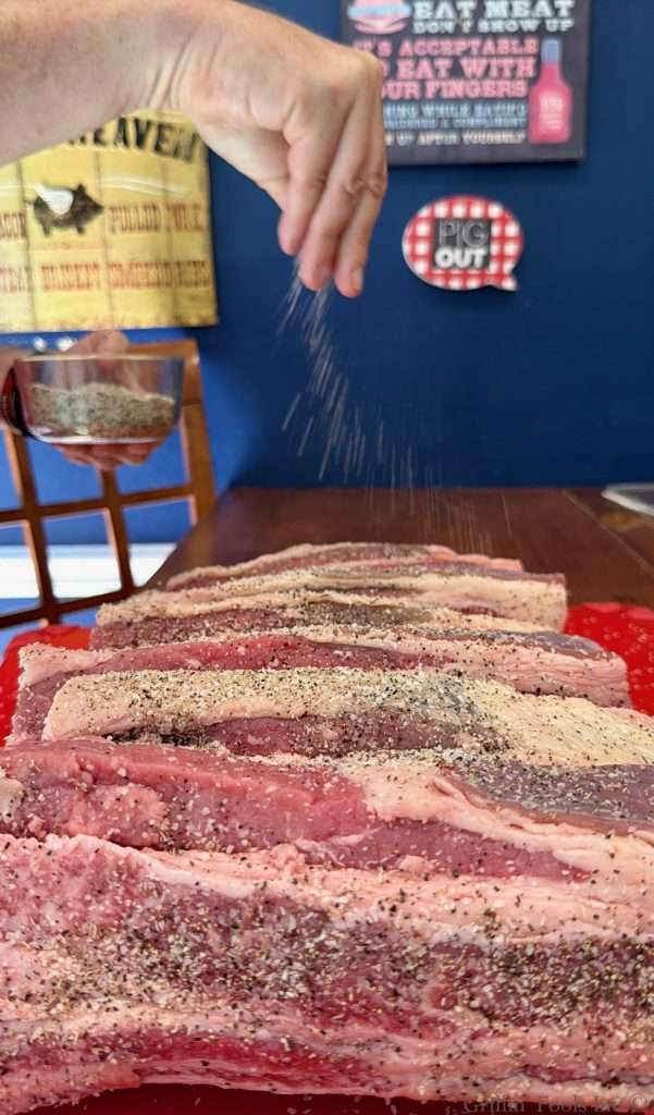 A man seasons raw beef ribs with salt pepper and garlic