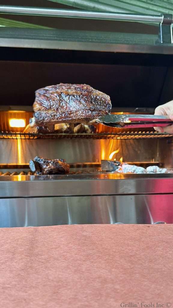 A man takes a beef rib off the grill towards peach butcher paper