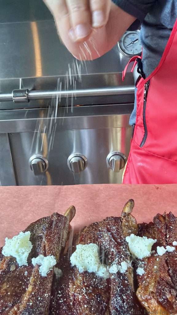 Adding seasoning to tallowed beef ribs on peach butcher paper