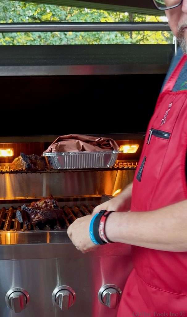 Beef ribs wrapped in butcher paper, in a couple disposable aluminum pans back on the grill
