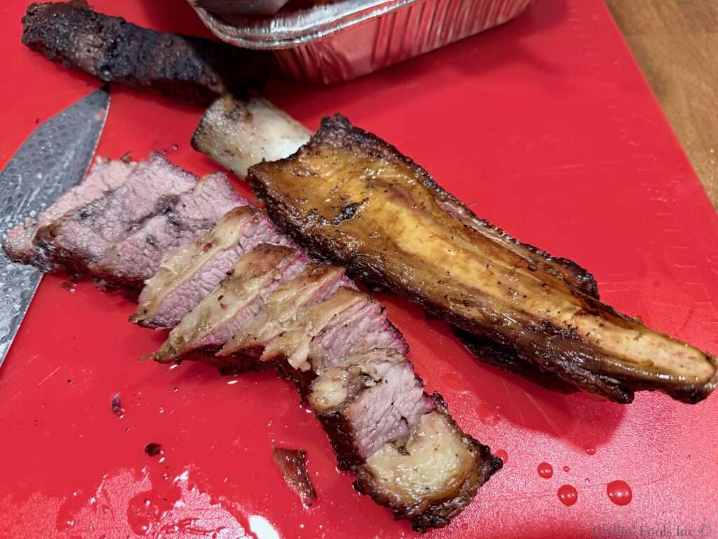 Sliced beef rib on a red cutting board with the bone nearby