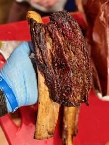 An individual beef ribs being held by a hand in a light blue nitrile glove