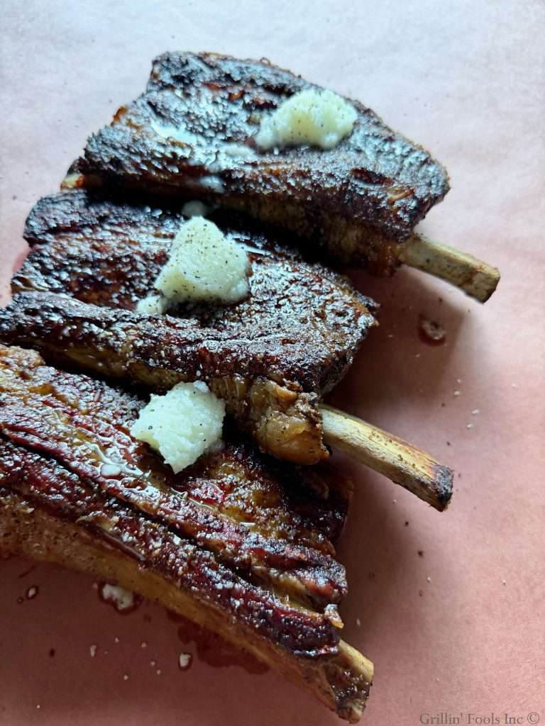 A beef ribs on the top rack of a charcoal grill