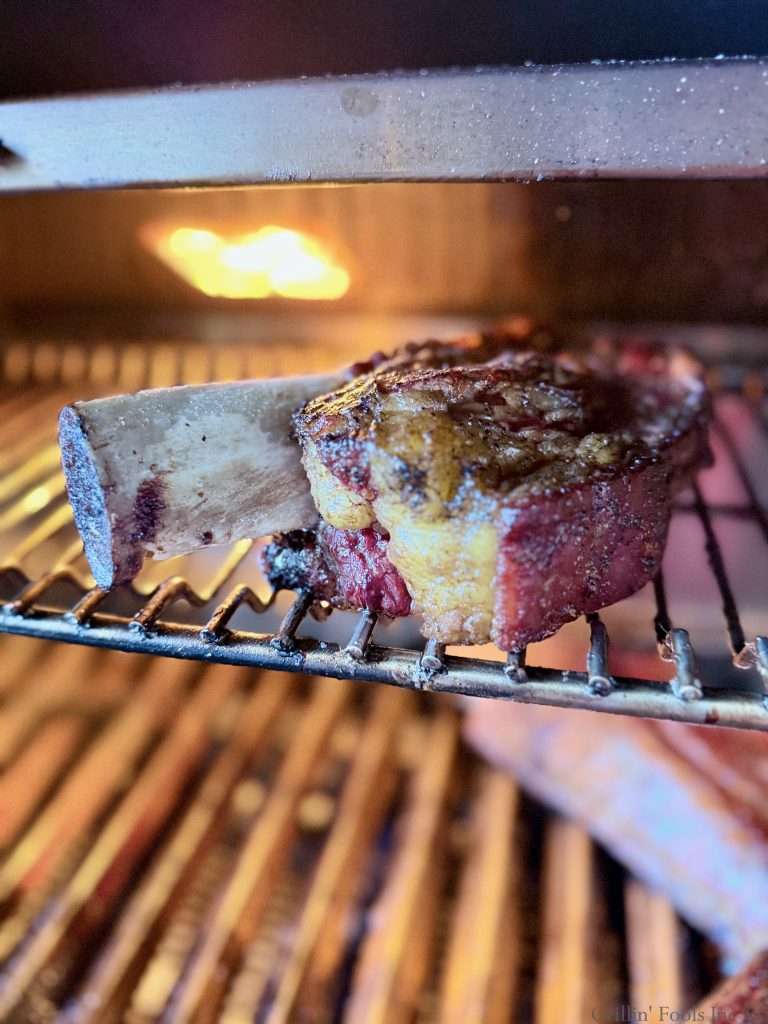 A beef ribs on the top rack of a charcoal grill