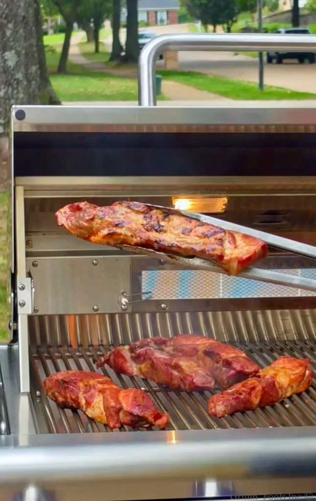 A country style rib with some char on it is held by tongs over a grill