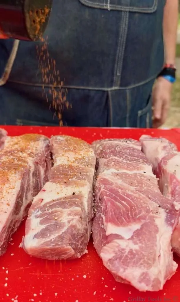 Seasoning the country style ribs in a red cutting board