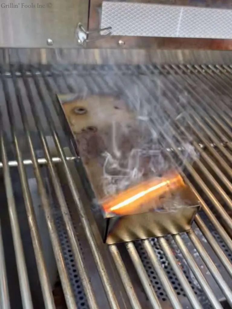 A smoking smoker box inside a gas grill