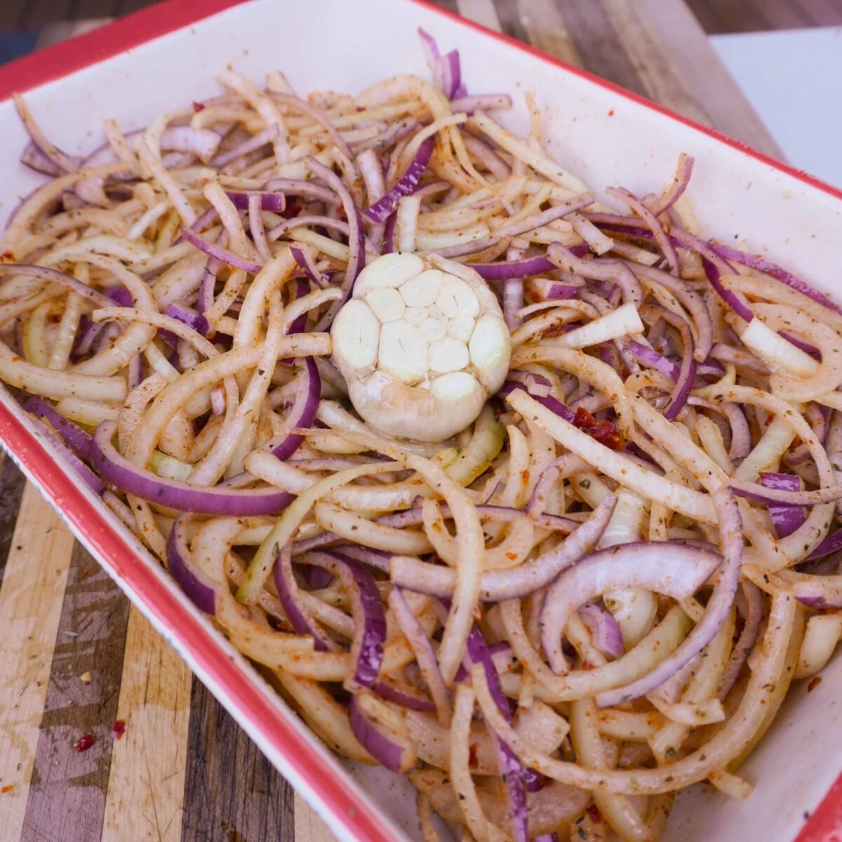 Sliced onions and garlic bulb in baking dish.