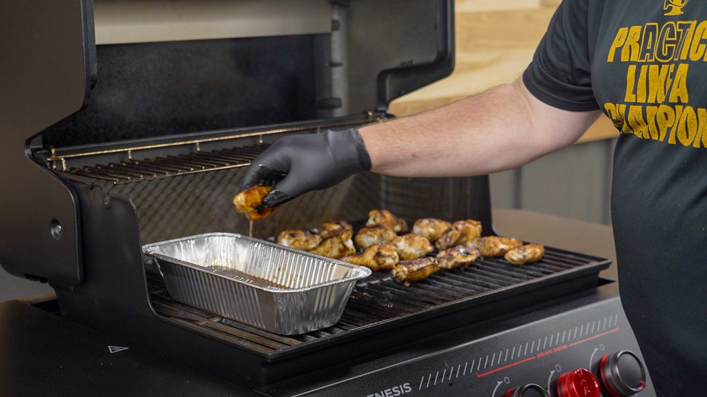 Dipping grilled chicken wings in barbecue sauce at the Weber Genesis E-330 Stealth