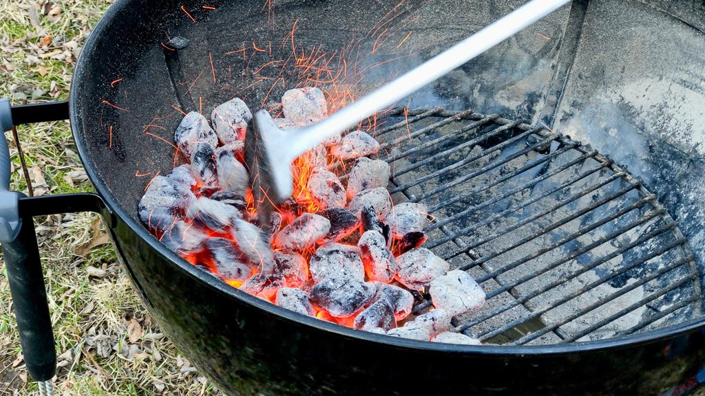 Spreading glowing charcoal across a kettle for direct grilling