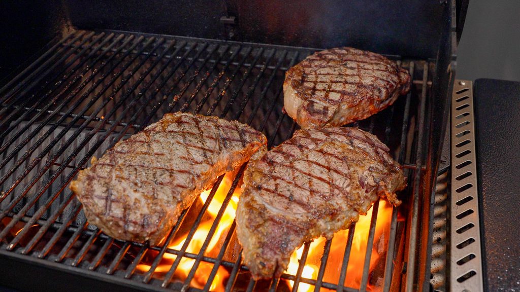 Ribeyes searing over open flame on the Weber Searwood