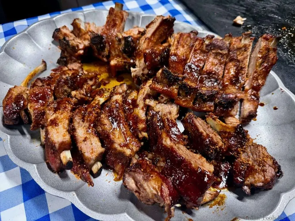 A platter with two slabs of saucy baby back ribs on a blue and white checked table cloth
