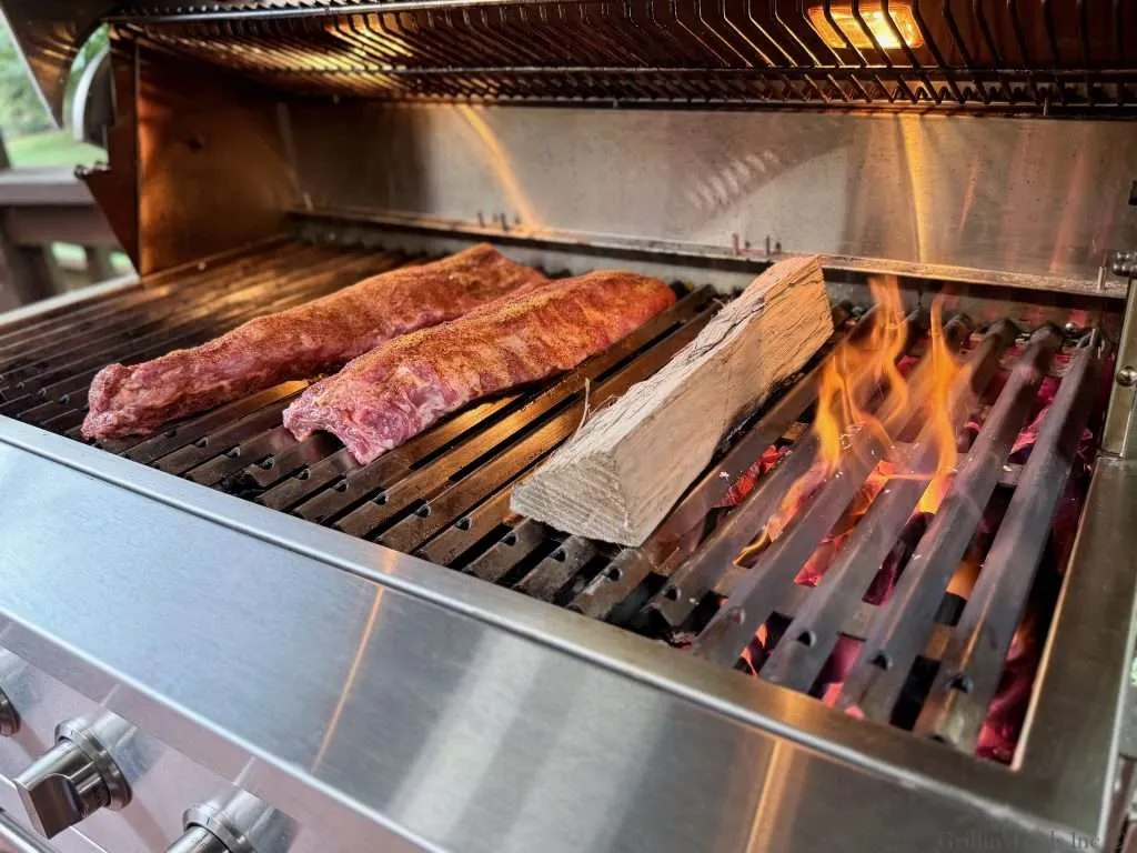 Two slabs of seasoned baby back ribs on one side of the grill with smoke wood and hot coals on the other side