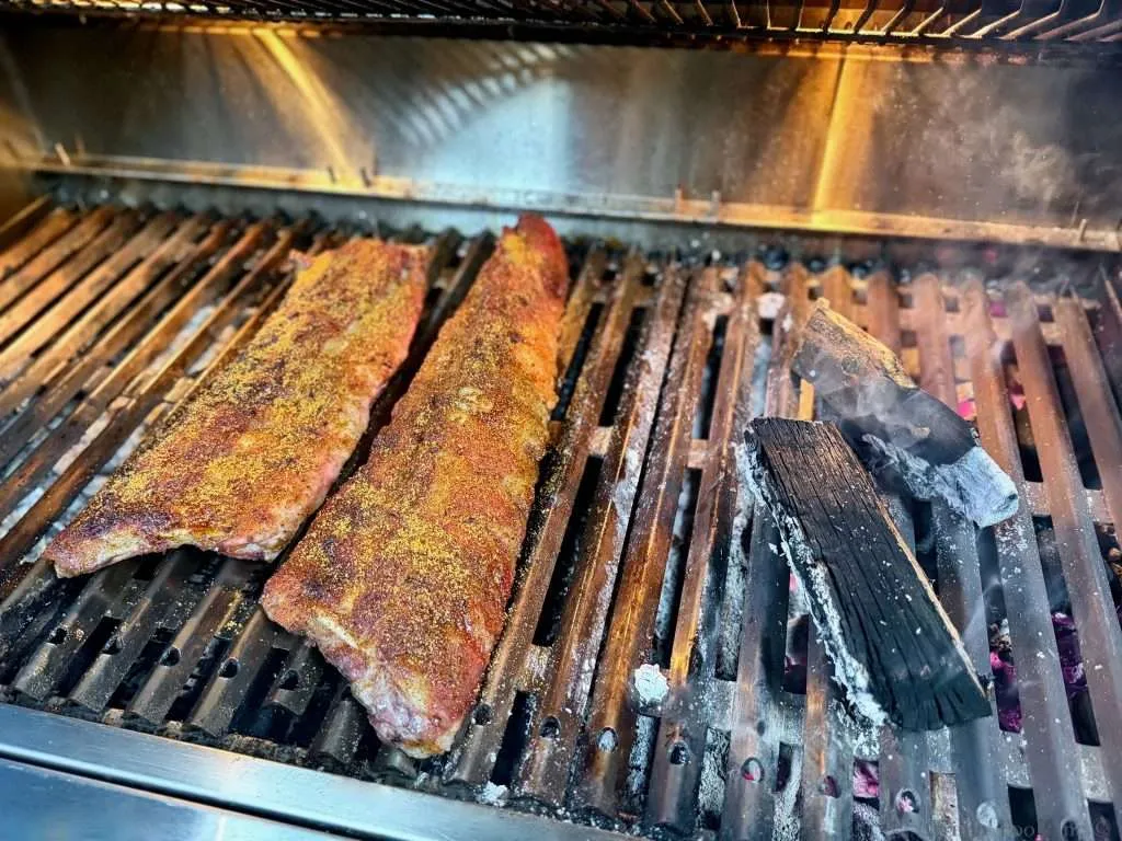 Freshly seasoned baby back ribs next to some nearly spent smoke wood