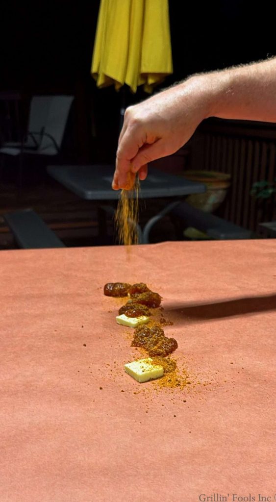 Sprinkling BBQ rub over three pats of butter and four teaspoons of apple butter all on a sheet of pink butcher paper