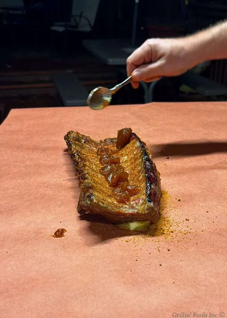 Spooning apple butter over the bone side of baby back ribs