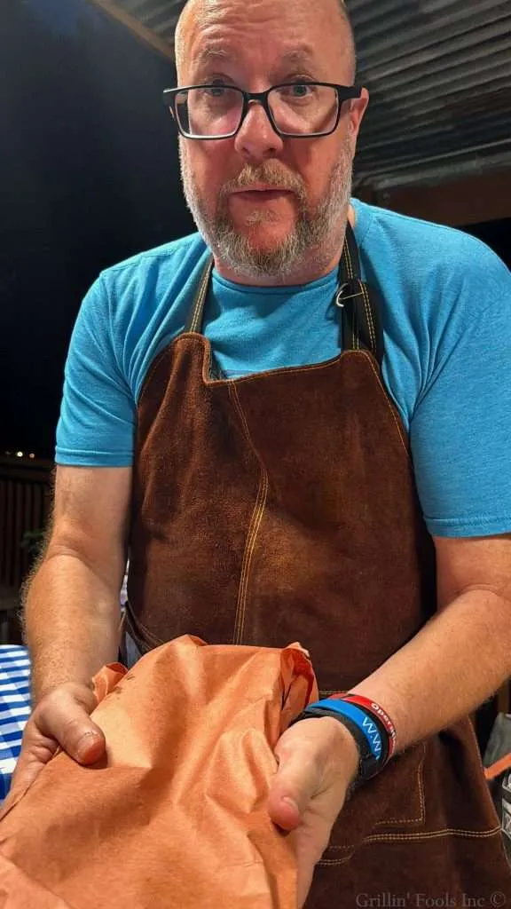 An incredibly handsome bearded man with glasses hold a slab of baby back ribs wrapped in pink butcher paper
