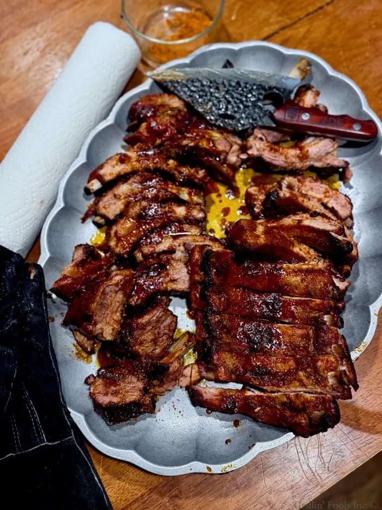 Two slabs of baby back ribs, carved into individual bones, slathered with an apple butter slurry and dusted with seasoning, all on a metal platter