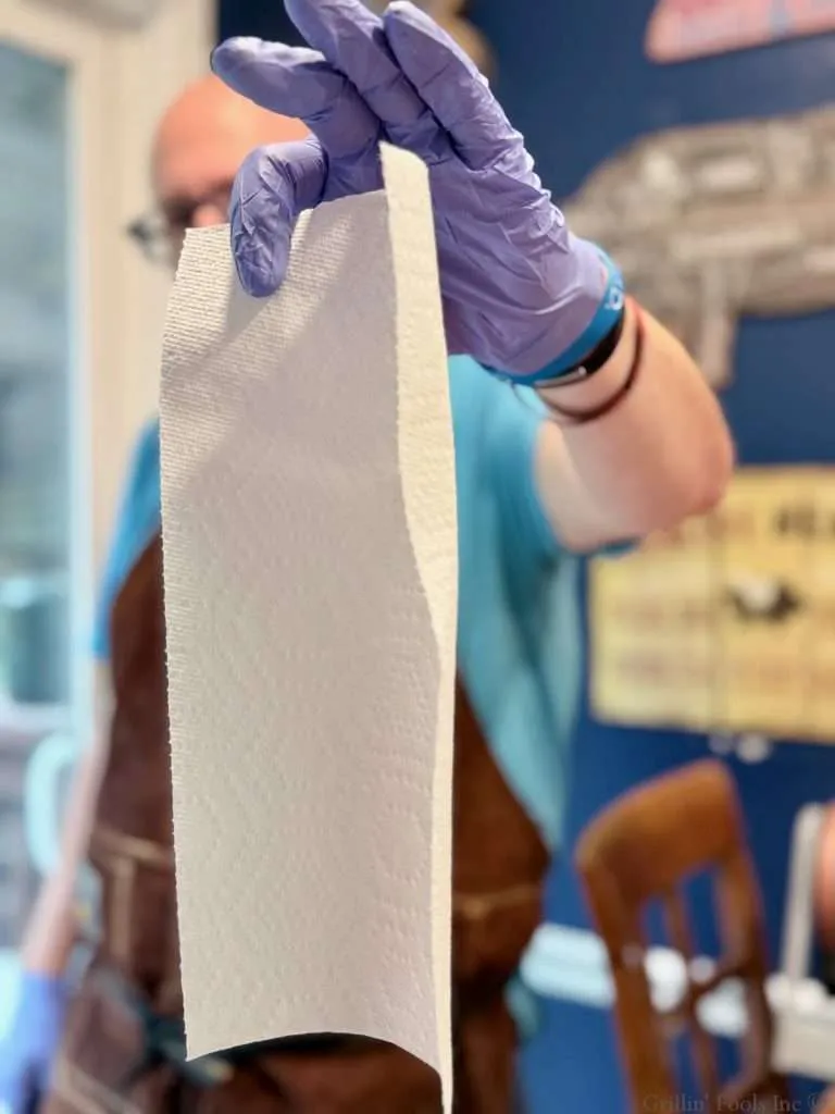 A man in light blue nitrile gloves holds up a half sheet of paper towel