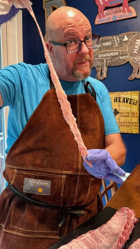 A super handsome man holds up the rib membrane after removing it from a slab of ribs
