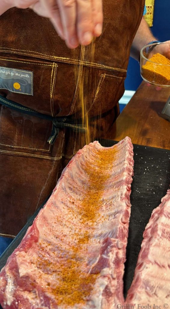 Seasoning the bone side of a slab of ribs with the BBQ rub